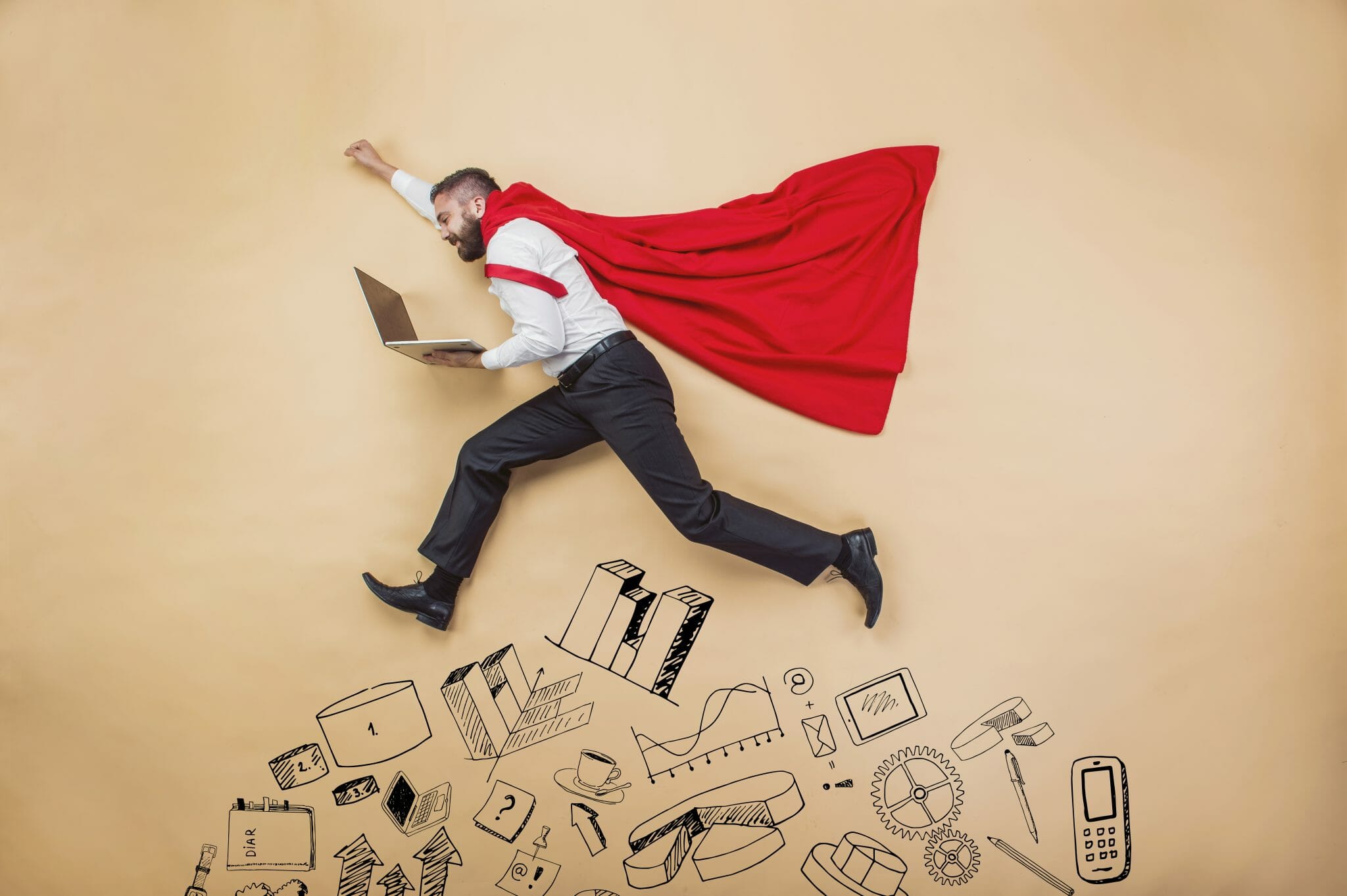 Man in cape holding computer leaping over various devleopment related graphics drawn on a wall