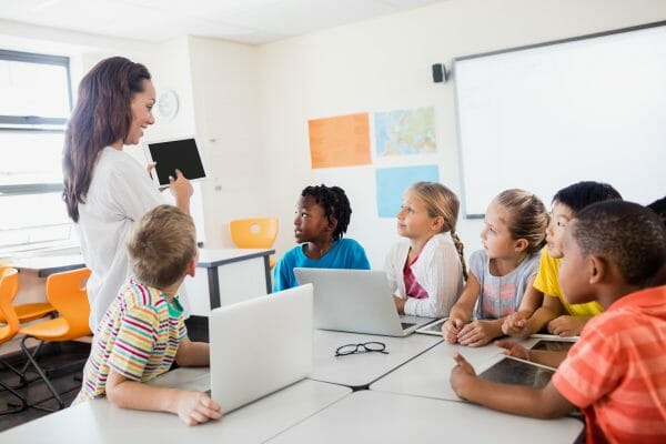 Teacher surrounded by students and showing educational material on a tablet